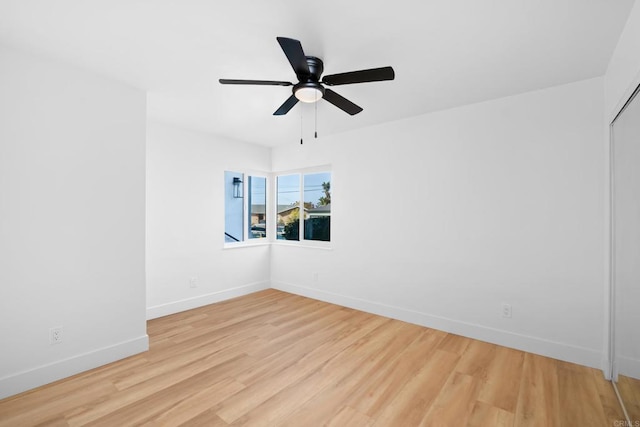 spare room with light wood-type flooring, a ceiling fan, and baseboards