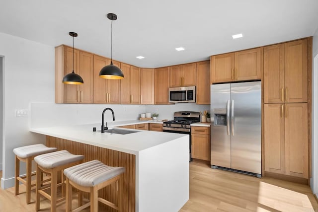 kitchen with stainless steel appliances, a peninsula, a sink, light countertops, and light wood finished floors