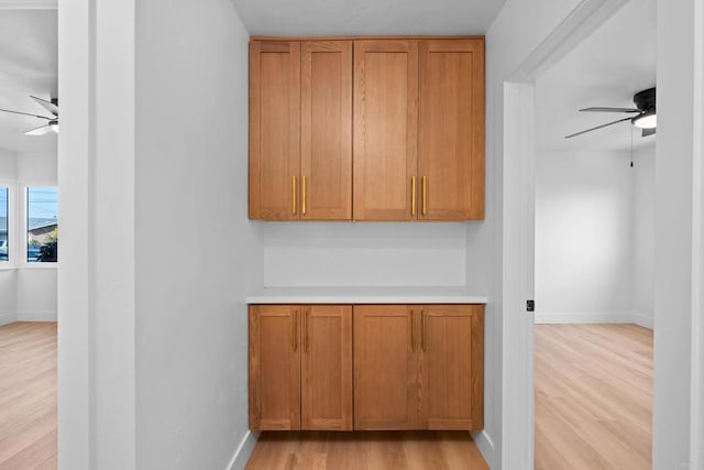 interior space with light wood-style floors, brown cabinets, ceiling fan, and baseboards