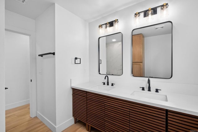 full bathroom with double vanity, wood finished floors, a sink, and baseboards