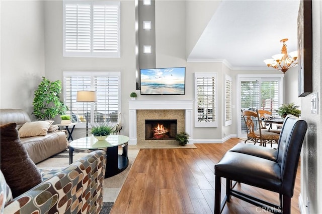 living room with a notable chandelier, a fireplace with flush hearth, ornamental molding, wood finished floors, and baseboards