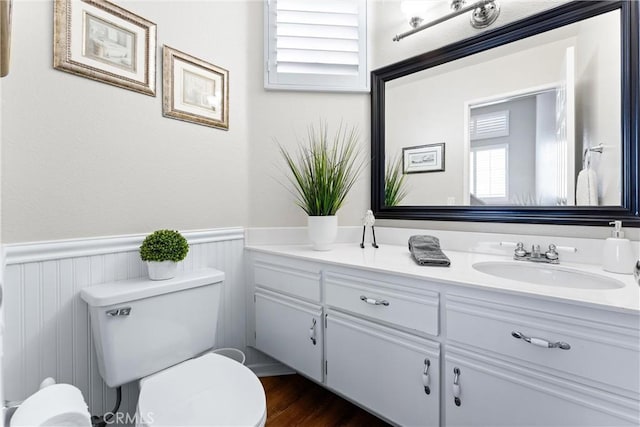 half bath with wood finished floors, wainscoting, vanity, and toilet