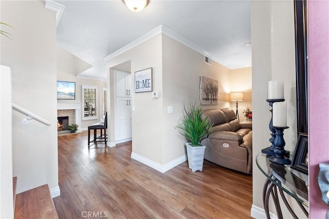 interior space featuring wood-type flooring, visible vents, ornamental molding, a glass covered fireplace, and baseboards