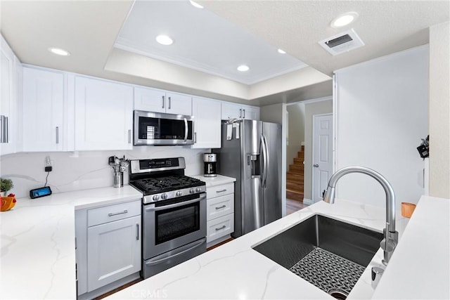 kitchen with a sink, visible vents, white cabinetry, appliances with stainless steel finishes, and a tray ceiling