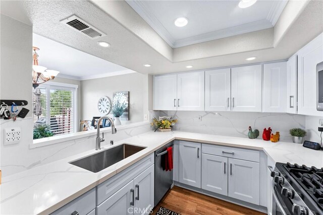 kitchen featuring wood finished floors, a sink, visible vents, ornamental molding, and appliances with stainless steel finishes