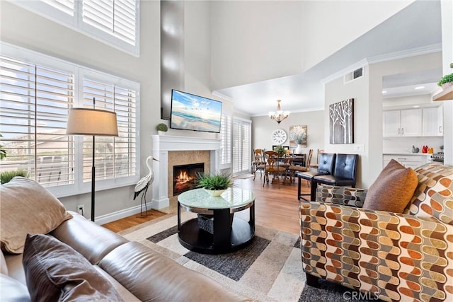 living area featuring crown molding, visible vents, a lit fireplace, light wood finished floors, and an inviting chandelier