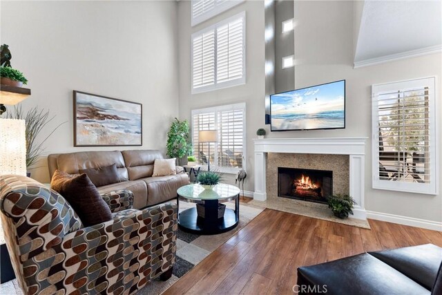 living room featuring a towering ceiling, a premium fireplace, ornamental molding, wood finished floors, and baseboards