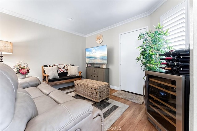 living room featuring ornamental molding, beverage cooler, baseboards, and light wood finished floors