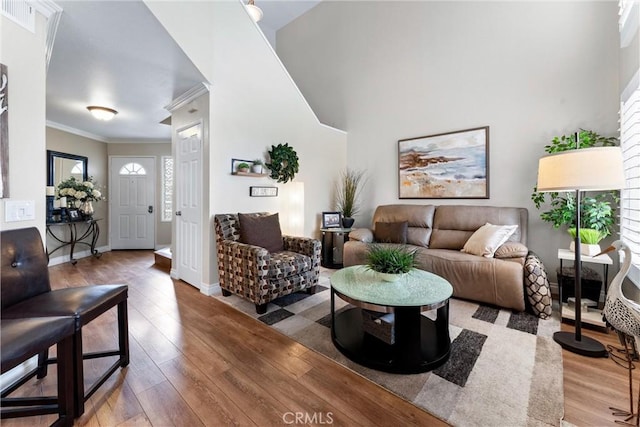 living area with a towering ceiling, baseboards, ornamental molding, and wood finished floors