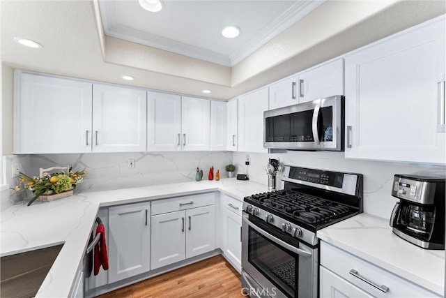 kitchen featuring appliances with stainless steel finishes, white cabinetry, ornamental molding, and light wood-style flooring