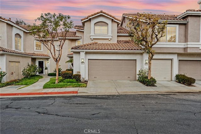 view of front of house featuring driveway, an attached garage, a tiled roof, and stucco siding