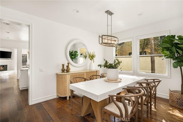 dining area with recessed lighting, dark wood-type flooring, baseboards, a glass covered fireplace, and an inviting chandelier