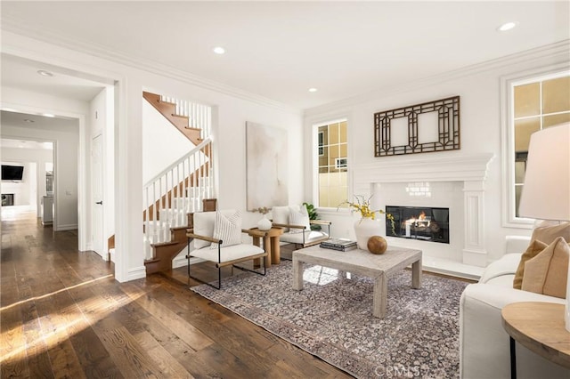 living area with stairs, dark wood finished floors, crown molding, and a glass covered fireplace