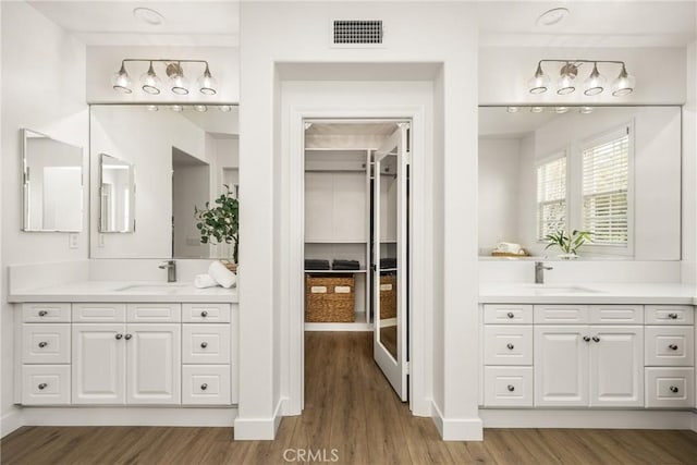 full bath with visible vents, two vanities, a sink, and wood finished floors