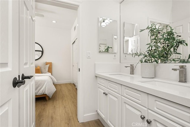 bathroom with double vanity, wood finished floors, a sink, and baseboards