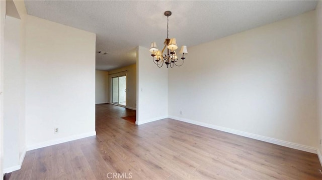 unfurnished room featuring a notable chandelier, a textured ceiling, baseboards, and wood finished floors