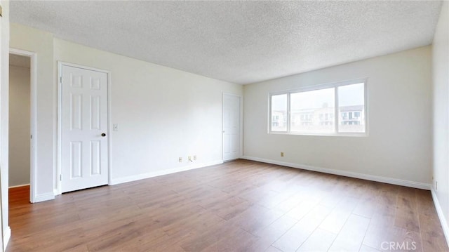 unfurnished room featuring a textured ceiling, wood finished floors, and baseboards