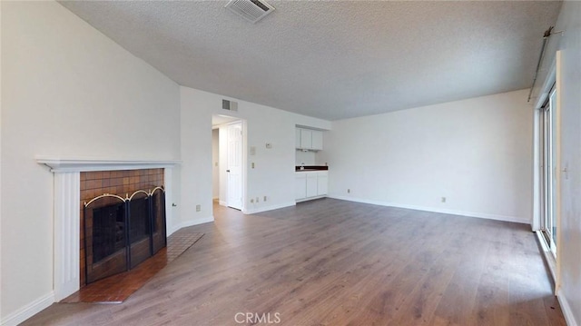 unfurnished living room featuring dark wood-style flooring, visible vents, a textured ceiling, and a tiled fireplace