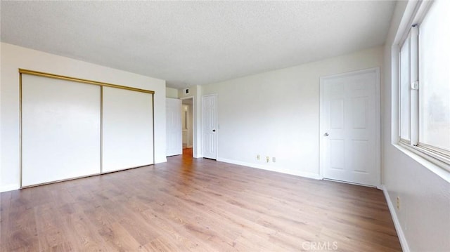 unfurnished bedroom with light wood-type flooring, a closet, a textured ceiling, and baseboards