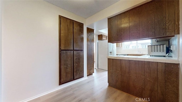 kitchen with tile countertops, light wood-style floors, white fridge with ice dispenser, and a textured ceiling