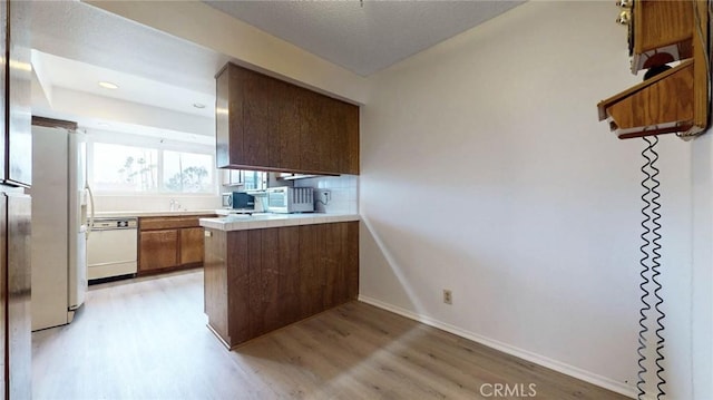 kitchen with white appliances, baseboards, brown cabinets, a peninsula, and light wood-style floors