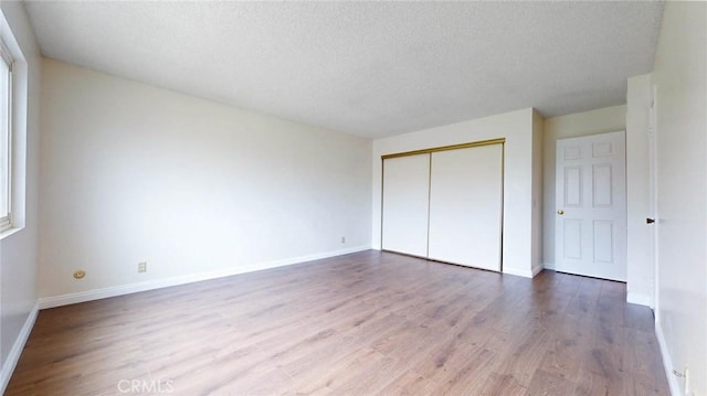 unfurnished bedroom with a textured ceiling, a closet, baseboards, and wood finished floors