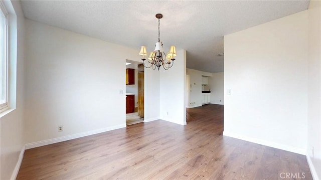 unfurnished dining area featuring baseboards, a textured ceiling, a chandelier, and wood finished floors