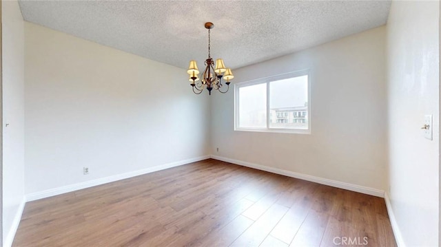 unfurnished room featuring an inviting chandelier, a textured ceiling, baseboards, and wood finished floors