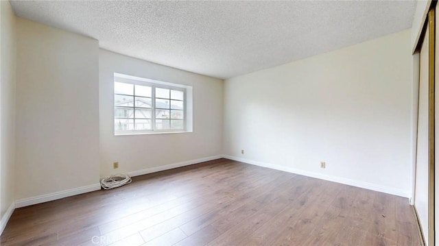 empty room with a textured ceiling, baseboards, and wood finished floors