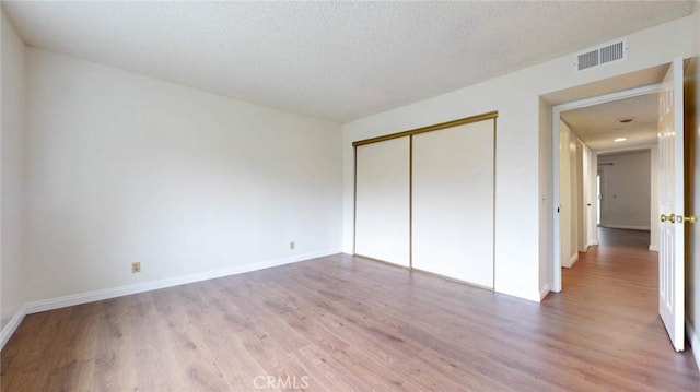 unfurnished bedroom with a closet, visible vents, light wood-style flooring, a textured ceiling, and baseboards