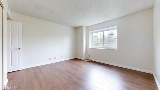 unfurnished room featuring a textured ceiling, baseboards, and wood finished floors