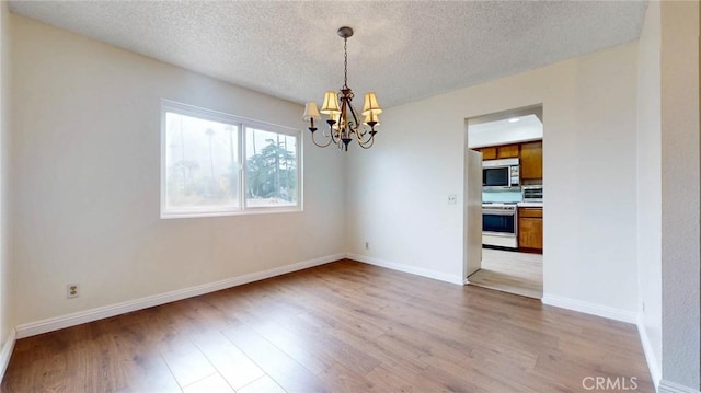 unfurnished dining area featuring baseboards, a textured ceiling, light wood-style flooring, and a notable chandelier