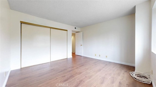 unfurnished bedroom with a textured ceiling, light wood finished floors, a closet, and visible vents