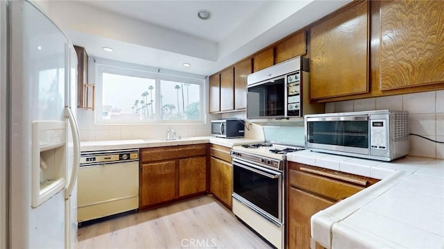 kitchen featuring tile countertops, white appliances, tasteful backsplash, and brown cabinetry