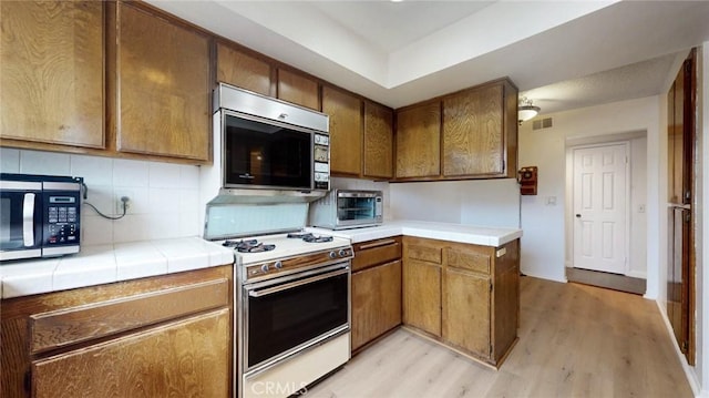 kitchen with light wood-style floors, tasteful backsplash, stainless steel microwave, and gas range gas stove