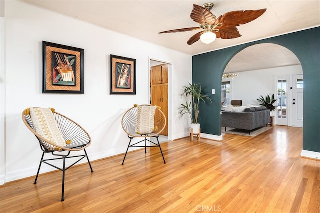 sitting room featuring ceiling fan with notable chandelier, baseboards, arched walkways, and light wood finished floors