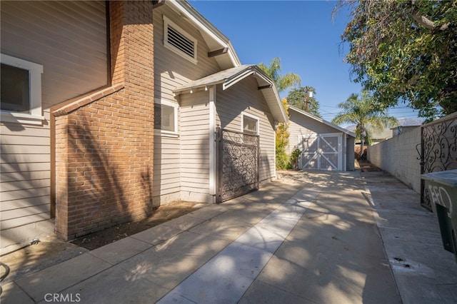 view of property exterior featuring driveway, fence, a shed, an outdoor structure, and brick siding