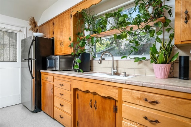 kitchen featuring brown cabinets, a sink, tile countertops, stainless steel appliances, and decorative backsplash