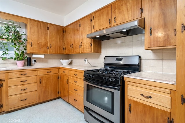 kitchen featuring backsplash, brown cabinetry, under cabinet range hood, and stainless steel gas range oven