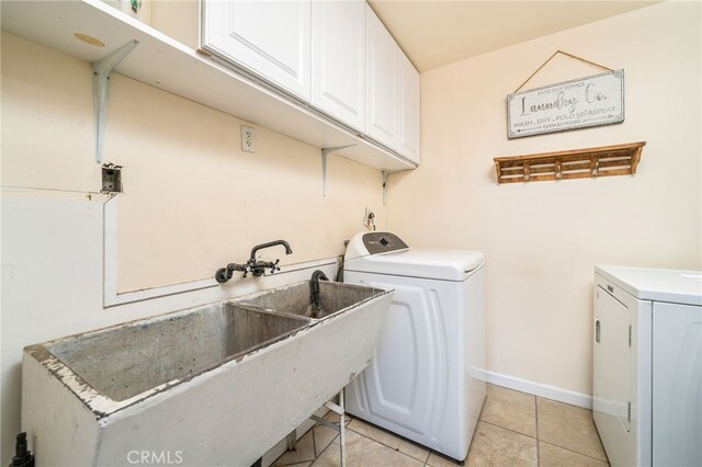 laundry room featuring baseboards, light tile patterned flooring, cabinet space, a sink, and independent washer and dryer