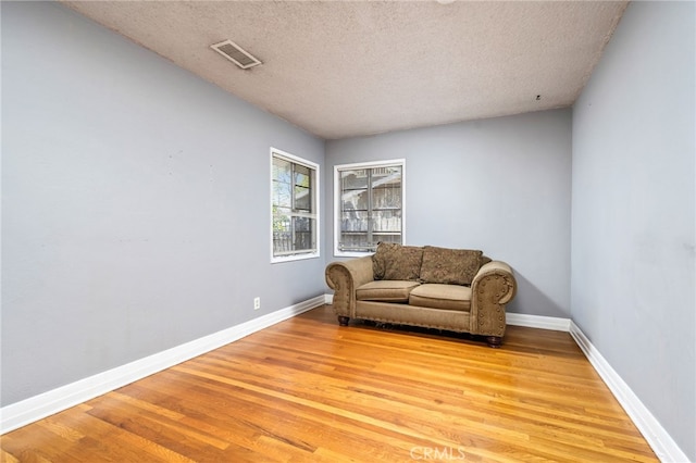 living area with visible vents, baseboards, a textured ceiling, and wood finished floors