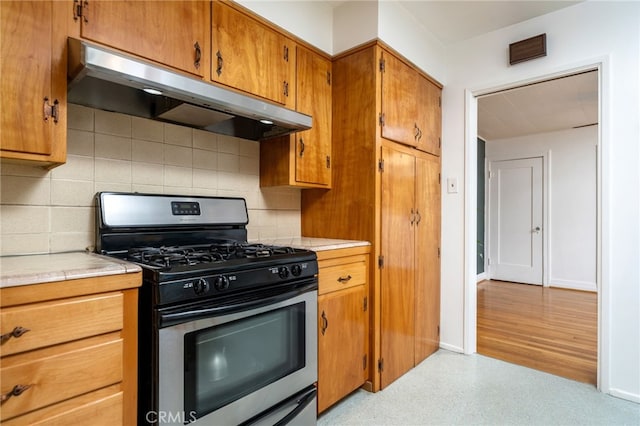 kitchen with backsplash, baseboards, under cabinet range hood, gas range, and brown cabinetry