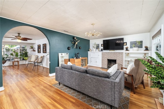 living room with light wood-type flooring, visible vents, ceiling fan with notable chandelier, arched walkways, and a fireplace