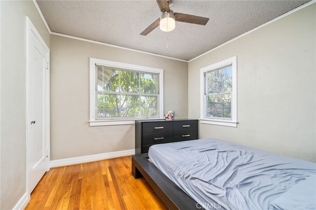 bedroom with baseboards, a textured ceiling, crown molding, and light wood finished floors