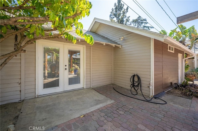 view of exterior entry with a patio area, french doors, and a shingled roof