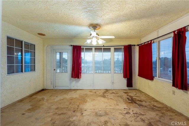 spare room featuring a textured ceiling, a textured wall, concrete floors, and ceiling fan