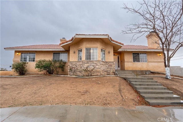 view of front of property with stone siding, a tile roof, a chimney, and stucco siding