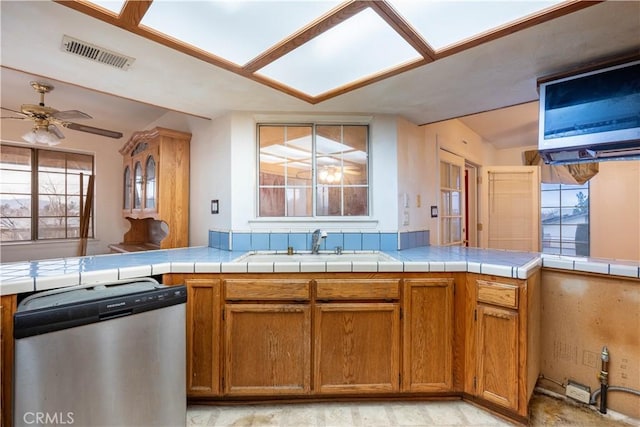 kitchen with ceiling fan, a sink, visible vents, stainless steel dishwasher, and brown cabinets