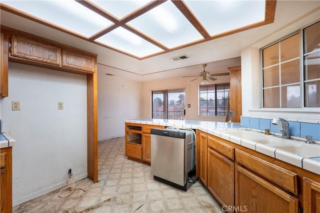 kitchen featuring visible vents, brown cabinetry, dishwasher, light floors, and a sink