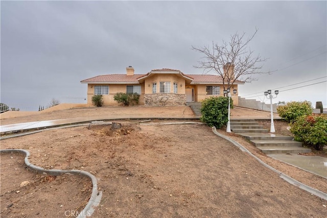 view of front of house featuring stone siding, a chimney, a tile roof, and stucco siding